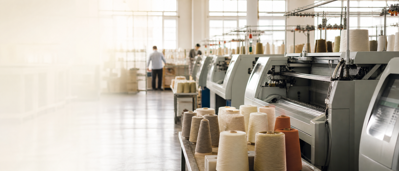 Computerized knitwear machines and yarn cones in a bright production workspace.