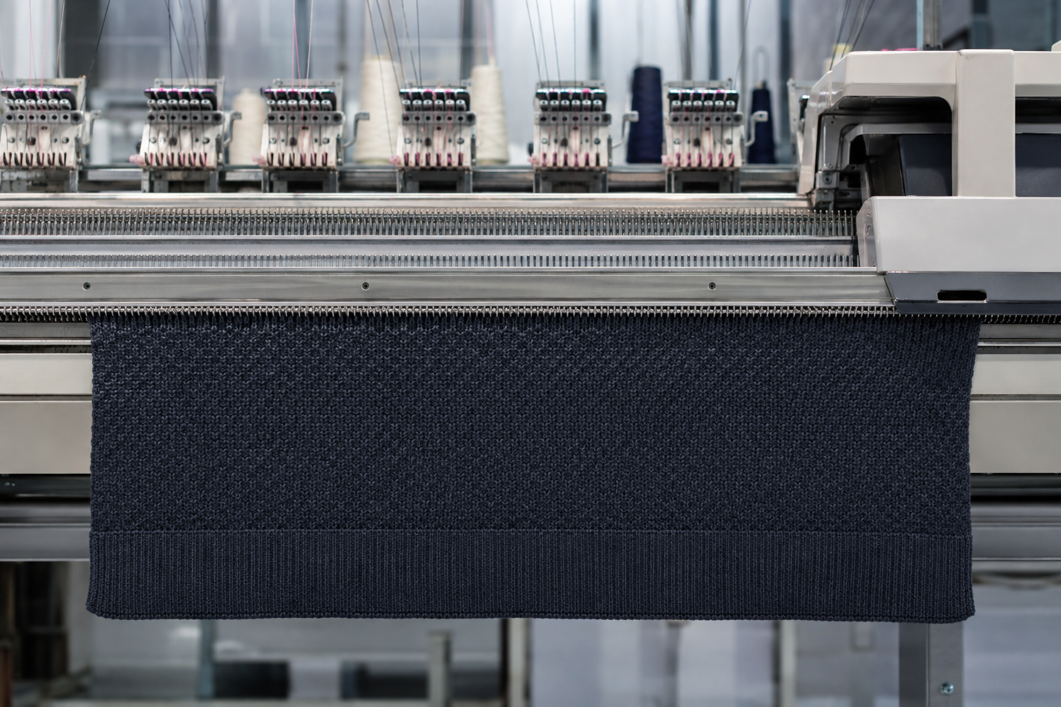 Computerized flat knitting machine producing a structured knitwear panel with a stable hem edge
